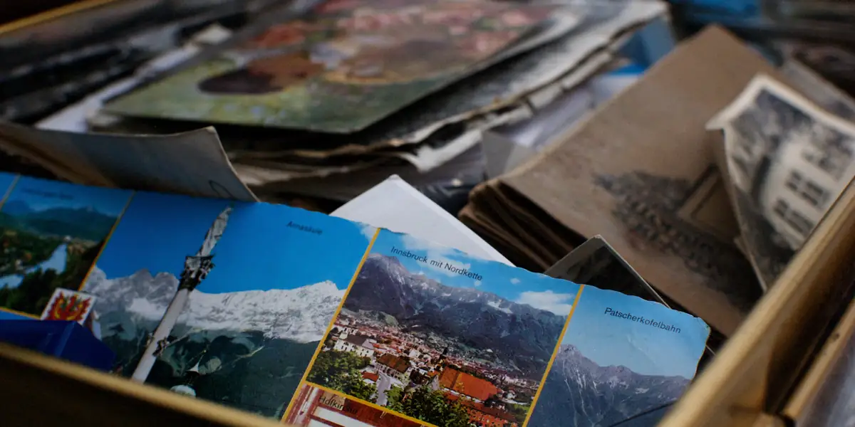 Scatola di cartone aperta piena di vecchie cartoline austriache; in cima una con Innsbruck mit Nordkette e riquadri più piccoli con le diciture Annasaeule, Patscherkofelbahn e Hofkirche