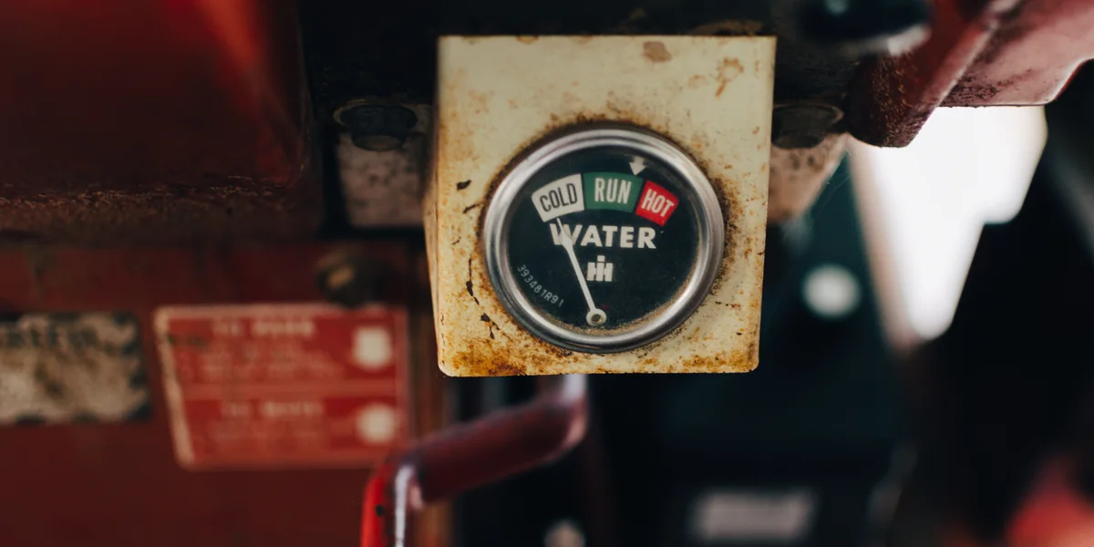 Rusted dashboard gauge on a farm machine, dial marked COLD, RUN and HOT under the word WATER, needle resting at the cold end