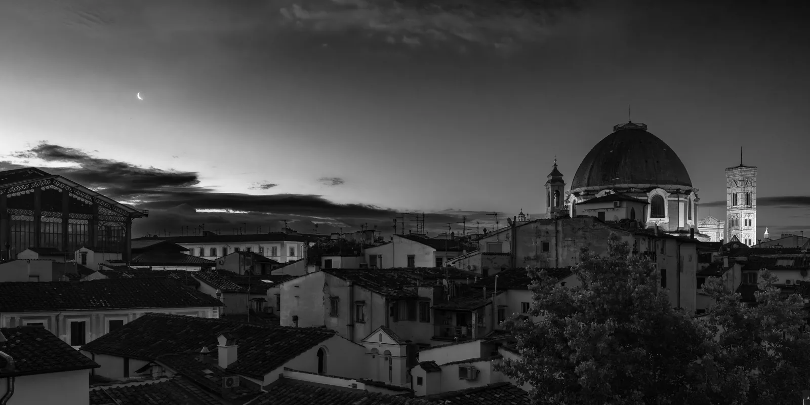 Black and white view of Florence at twilight, with the cathedral dome, Giotto's bell tower and the city rooftops under a thin crescent moon