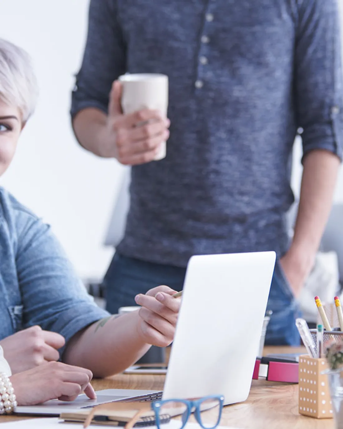 Two people at a desk with an open laptop and a cup of coffee